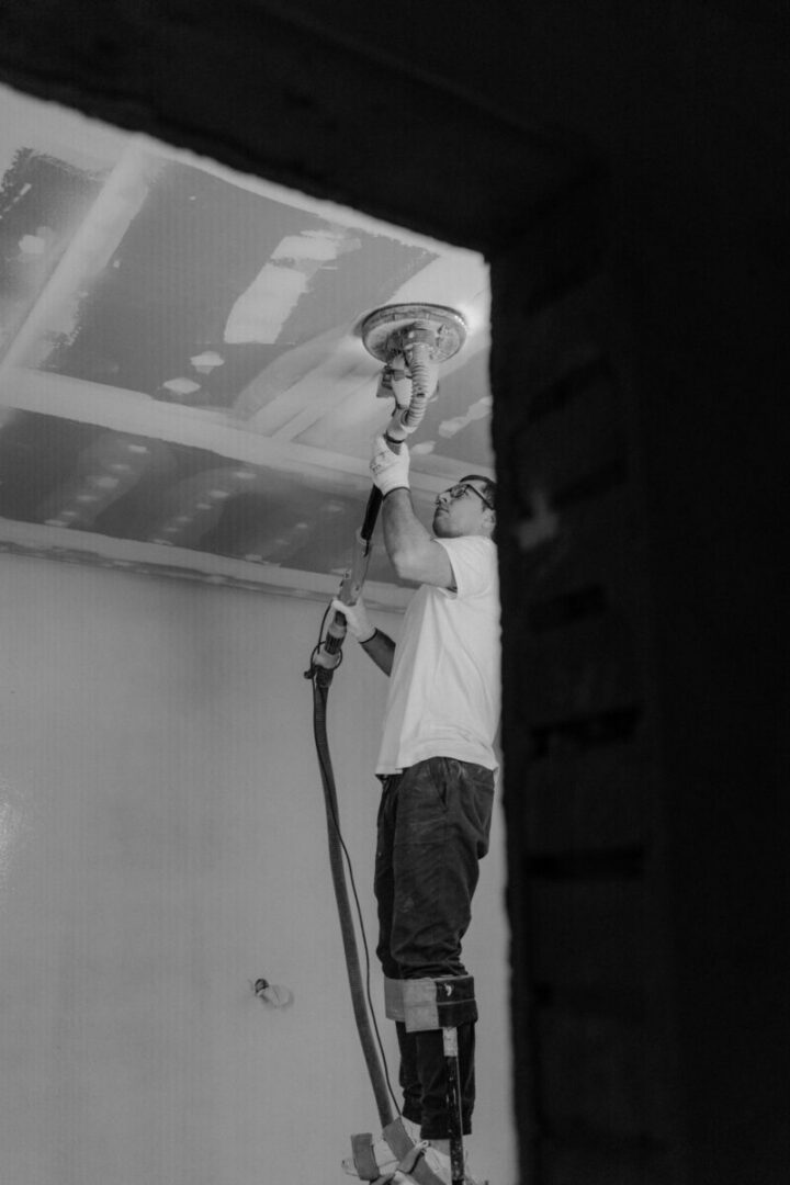 Man sanding the ceiling during a house renovation in black-and-white.